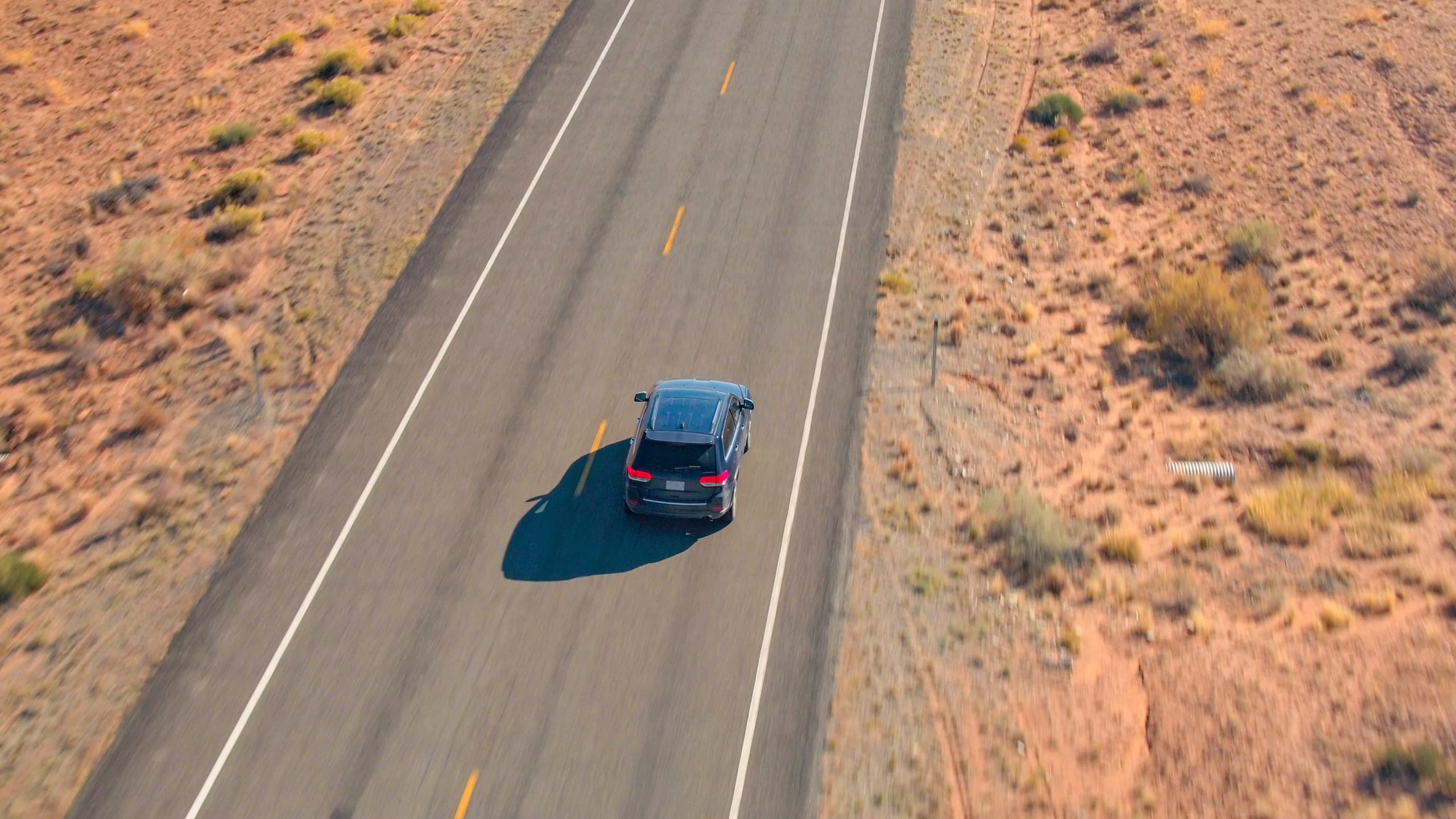 Expedition SUV on an empty desert road, photographed from the air in bright daylight